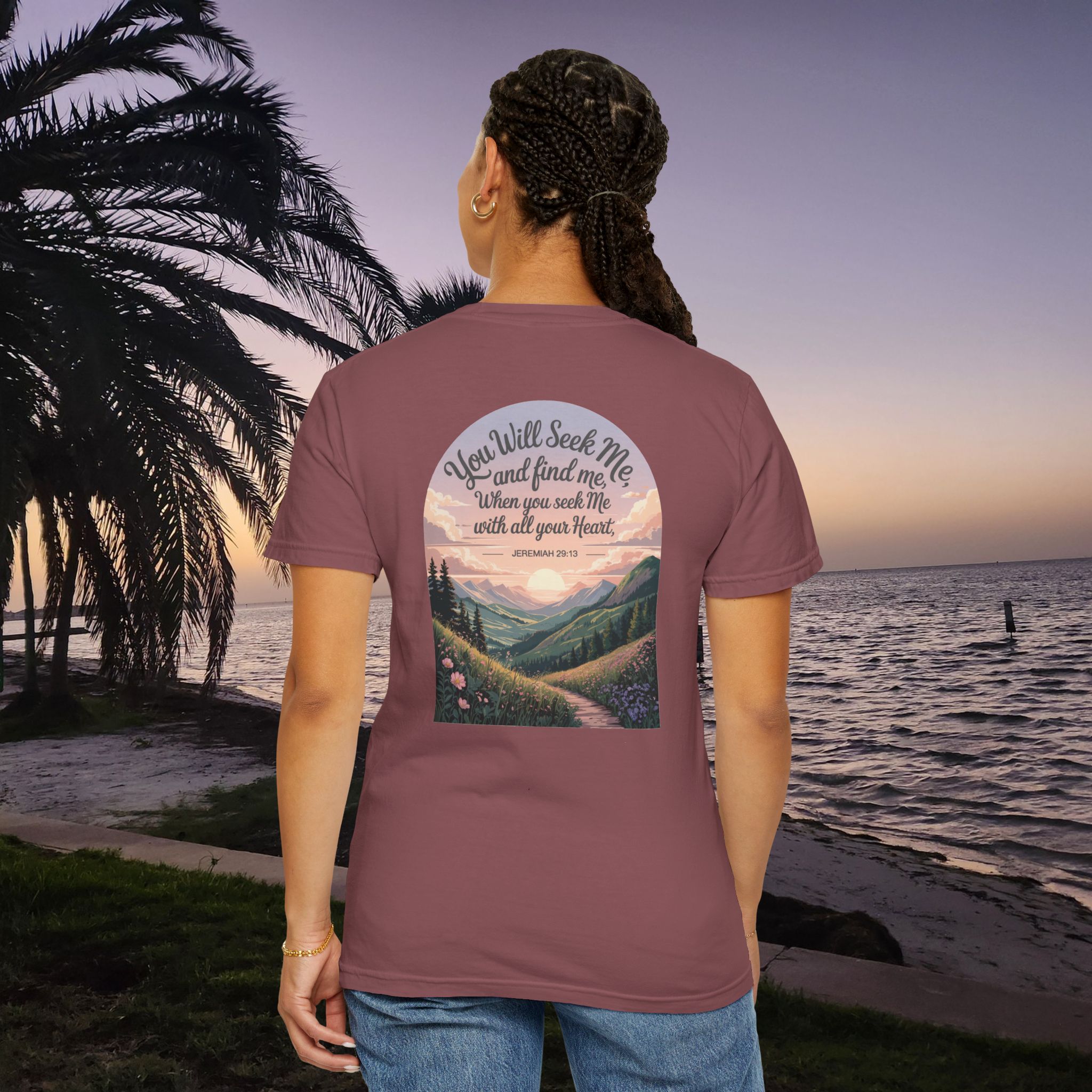 Red Christian t-shirt with Jeremiah 29:13 scripture, mountain valley, and sunset graphic, worn by a person in a serene beach setting.