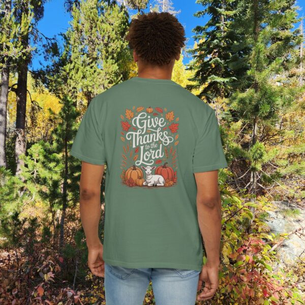 Model in a woods setting wearing a Green Give Thanks to the Lord t-shirt with Thanksgiving design showing a lamb, pumpkins, and fall leaves.