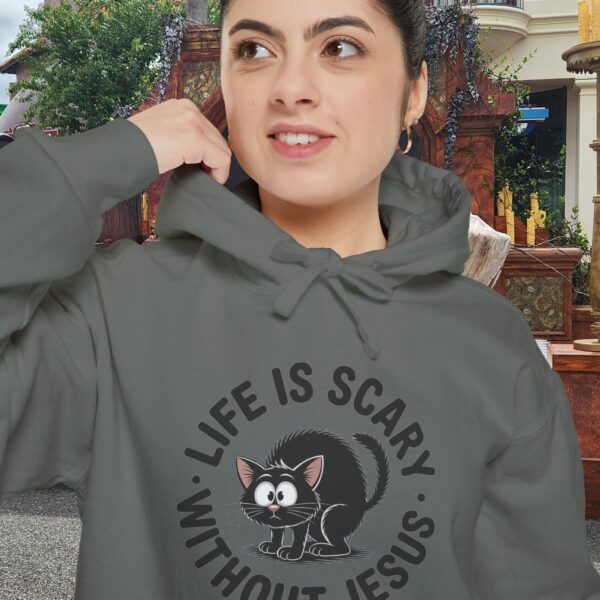 Model on a Halloween set wearing a gray Life is Scary Without Jesus Halloween Hoodie, design showing a cute frightened black cat.