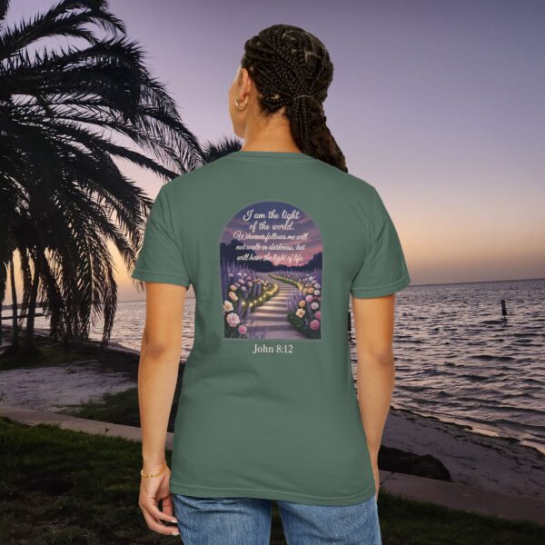 Green Christian t-shirt with John 8:12 scripture, lit stairway path with flowers and sunset design, worn by a person standing on a sunset beach.