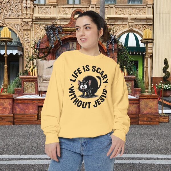 Model on a Halloween set wearing a yellow Life is Scary Without Jesus Halloween Sweatshirt, design showing a cute frightened black cat.