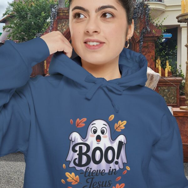 Model on a Halloween set wearing a blue Boo! -lieve in Jesus Halloween Hoodie, design showing a cute ghost with fall leaves.