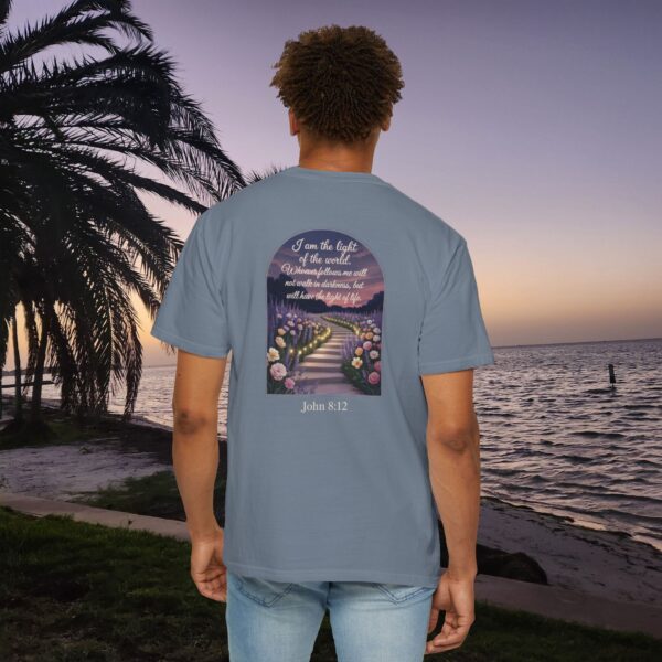 Blue Christian t-shirt with John 8:12 scripture, lit stairway path with flowers and sunset design, worn by a person standing on a sunset beach.